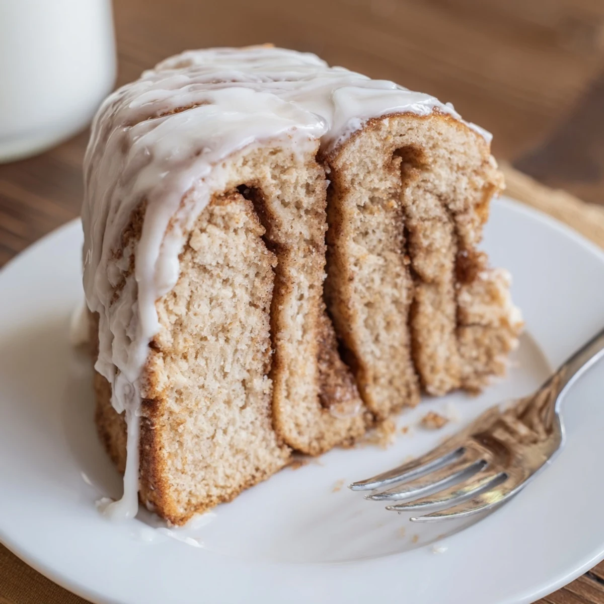 Golden swirled cinnamon roll cake drizzled with white vanilla glaze on a serving plate