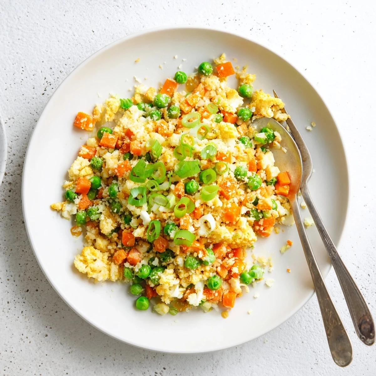 Golden cauliflower fried rice with colorful peas, carrots, and scrambled eggs in a serving bowl