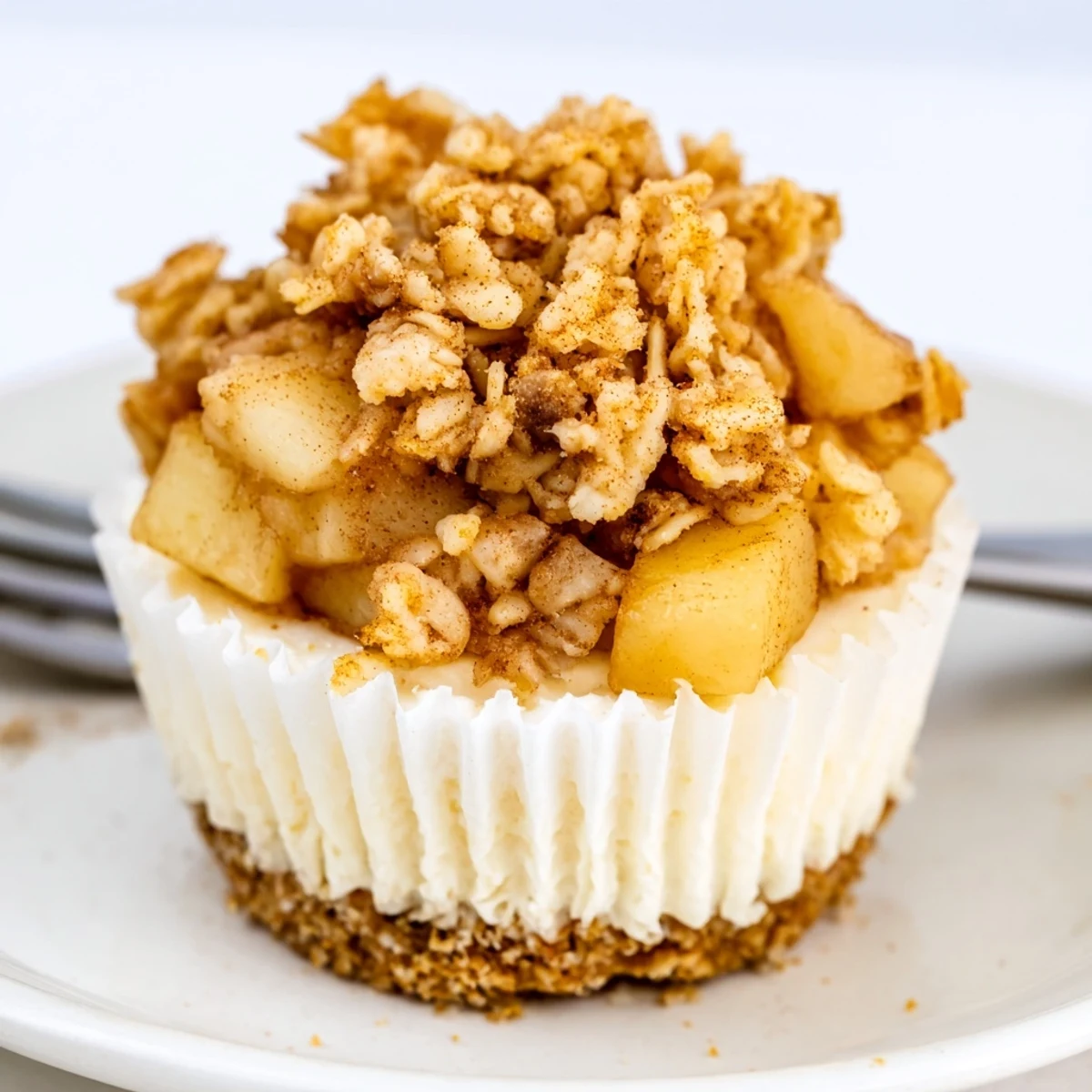 Individual cheesecakes topped with warm cinnamon apples and crispy crumble on white plate