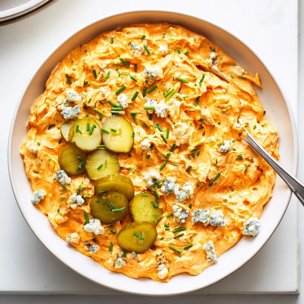 Tangy buffalo pickle dip topped with cheddar cheese and fresh chives in a rustic bowl
