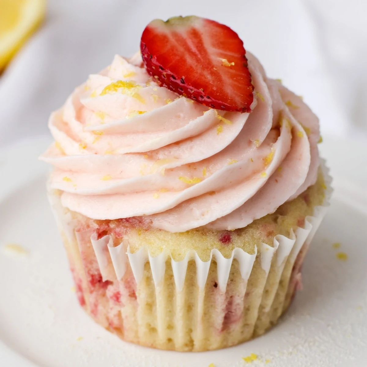 Pink frosted strawberry lemonade cupcakes topped with swirls of tangy buttercream on a rustic serving plate