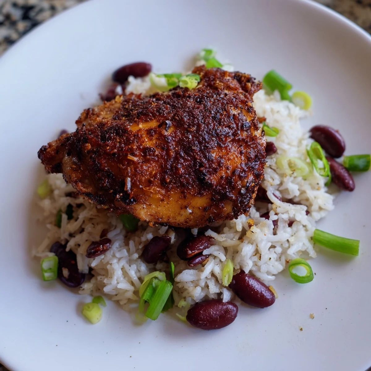 Golden brown jerk-marinated chicken thighs resting atop fluffy coconut rice with kidney beans