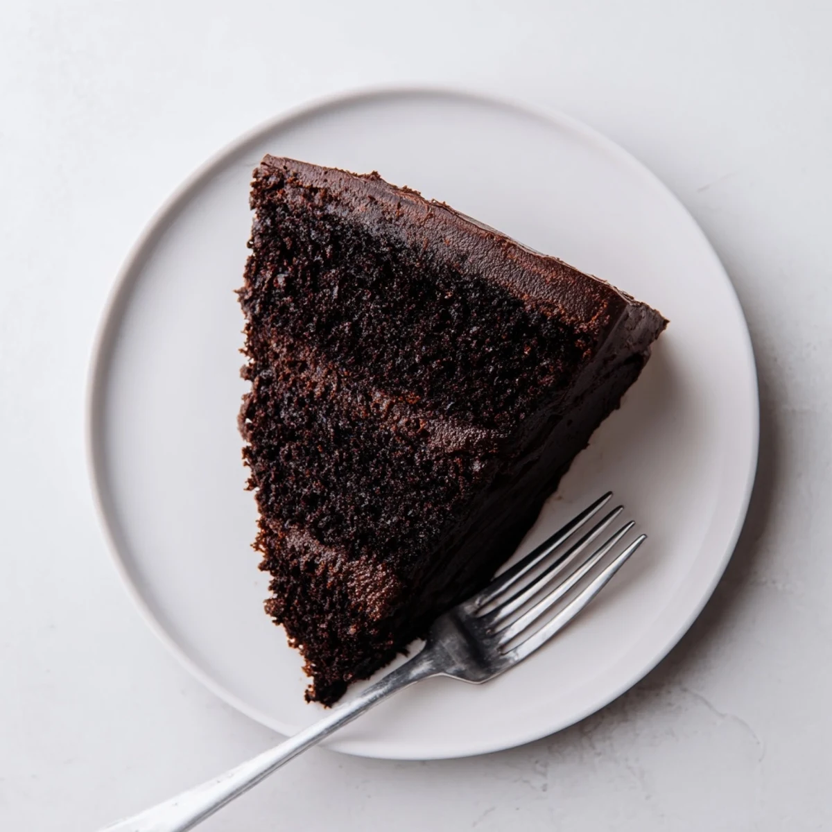 Slice of tender chocolate mayonnaise cake showing the dark crumb texture on a rustic wooden board