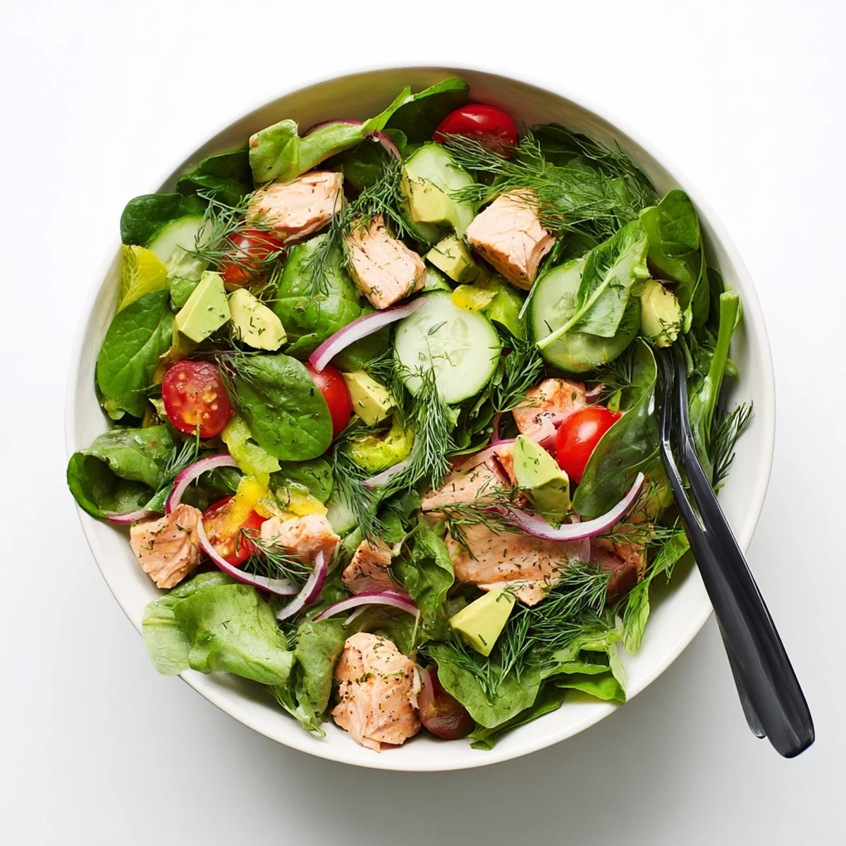 Fresh baked salmon chunks atop mixed greens with cherry tomatoes and creamy avocado in a lemon dill dressing