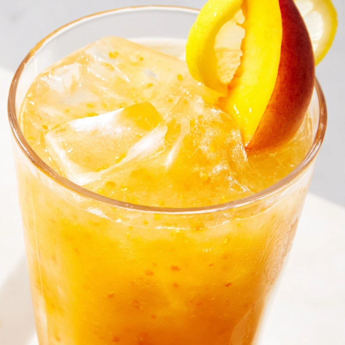 Fresh peach lemonade drink in a clear glass pitcher with floating peach slices and ice