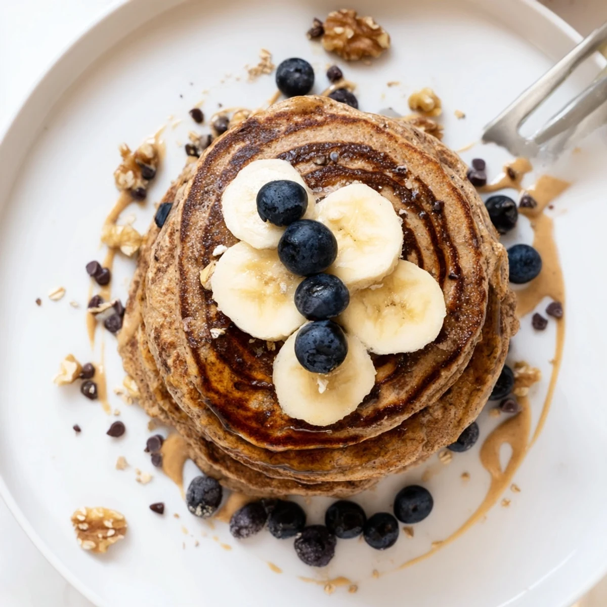 Stack of golden Protein Banana Pancakes topped with sliced bananas and syrup