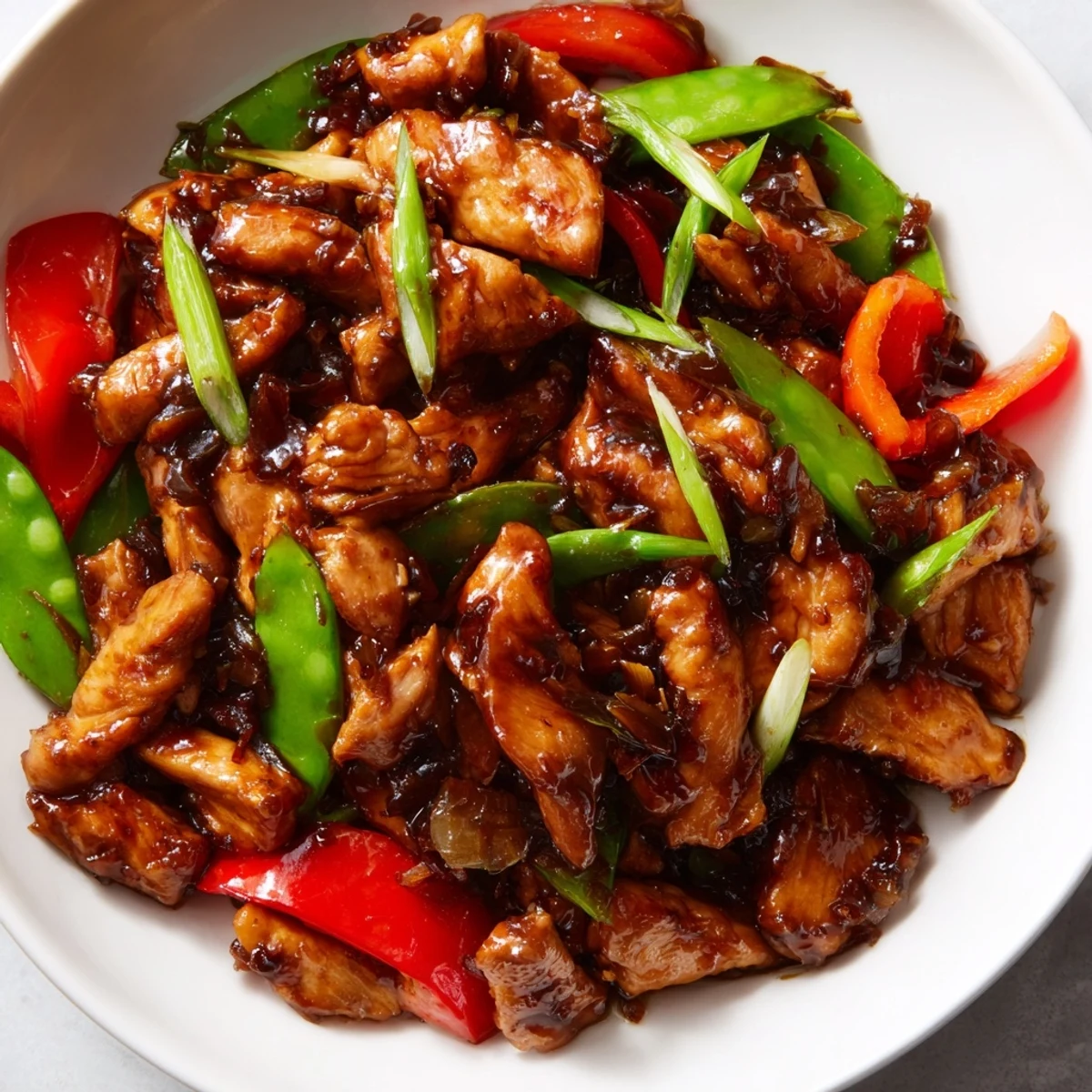Glossy stir-fried Chinese garlic chicken sizzling with red peppers and snow peas