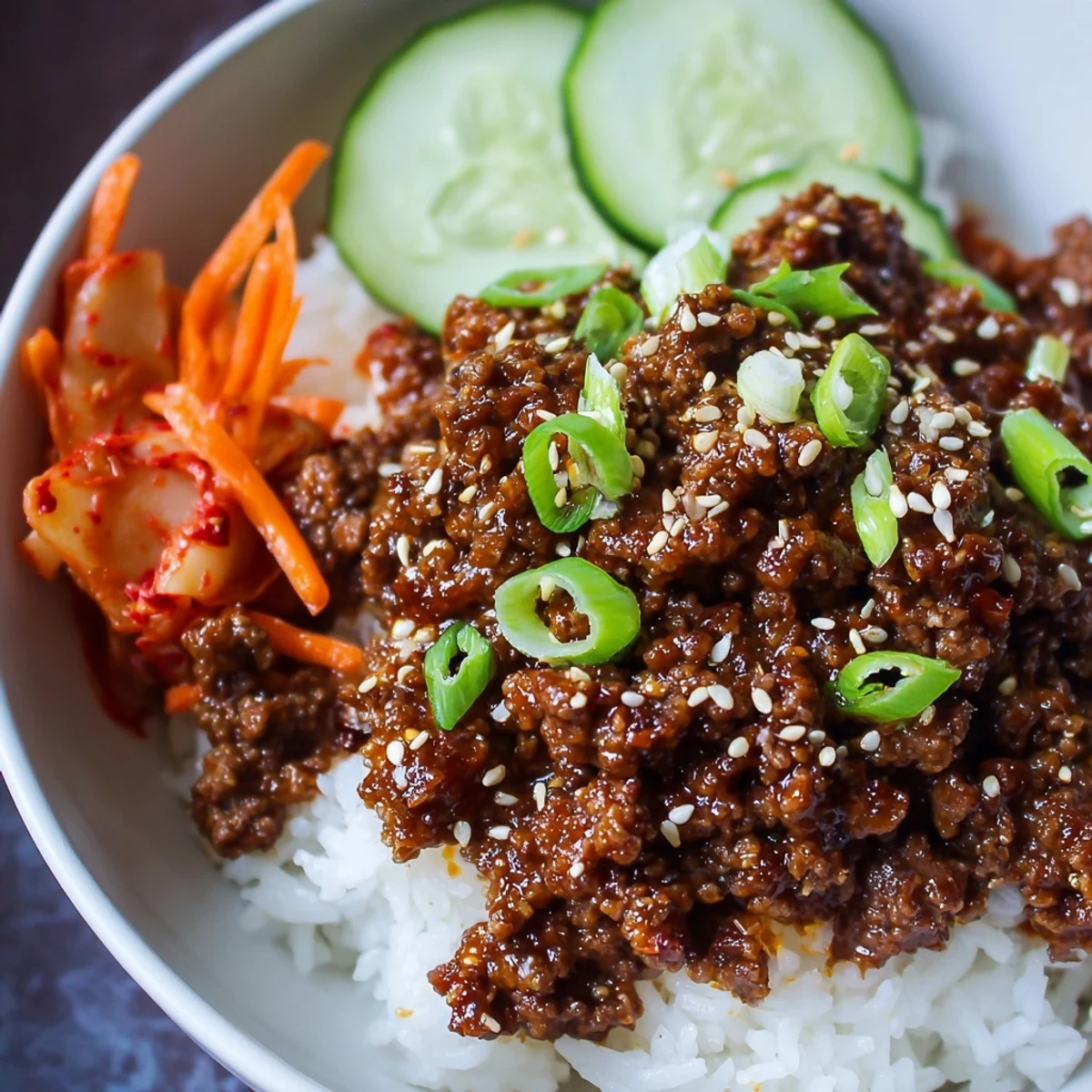 Savory Korean ground beef bowl topped with sesame seeds, green onions, and fresh cucumber