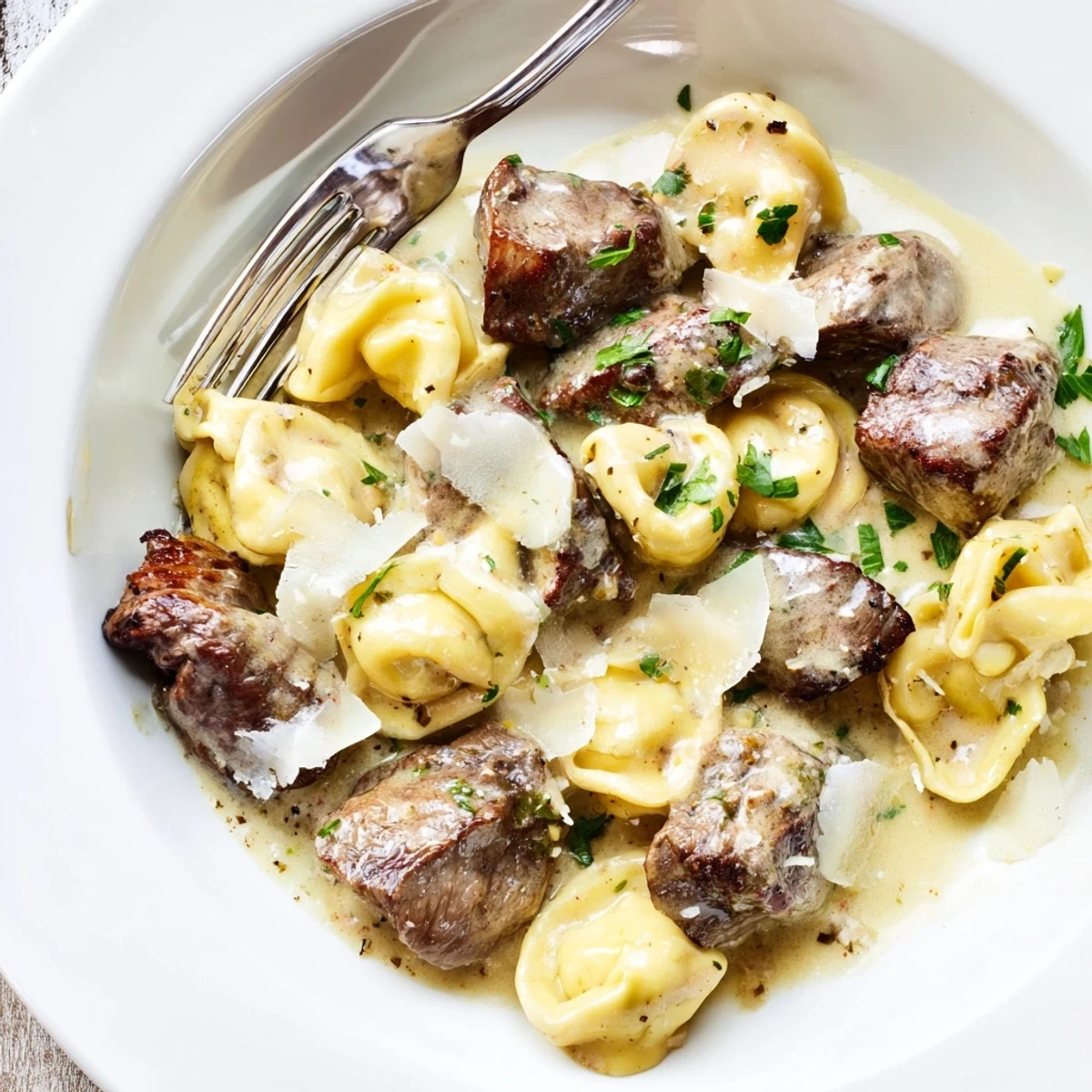 Creamy garlic steak tortellini plated with tender beef and parmesan coating pasta pieces.